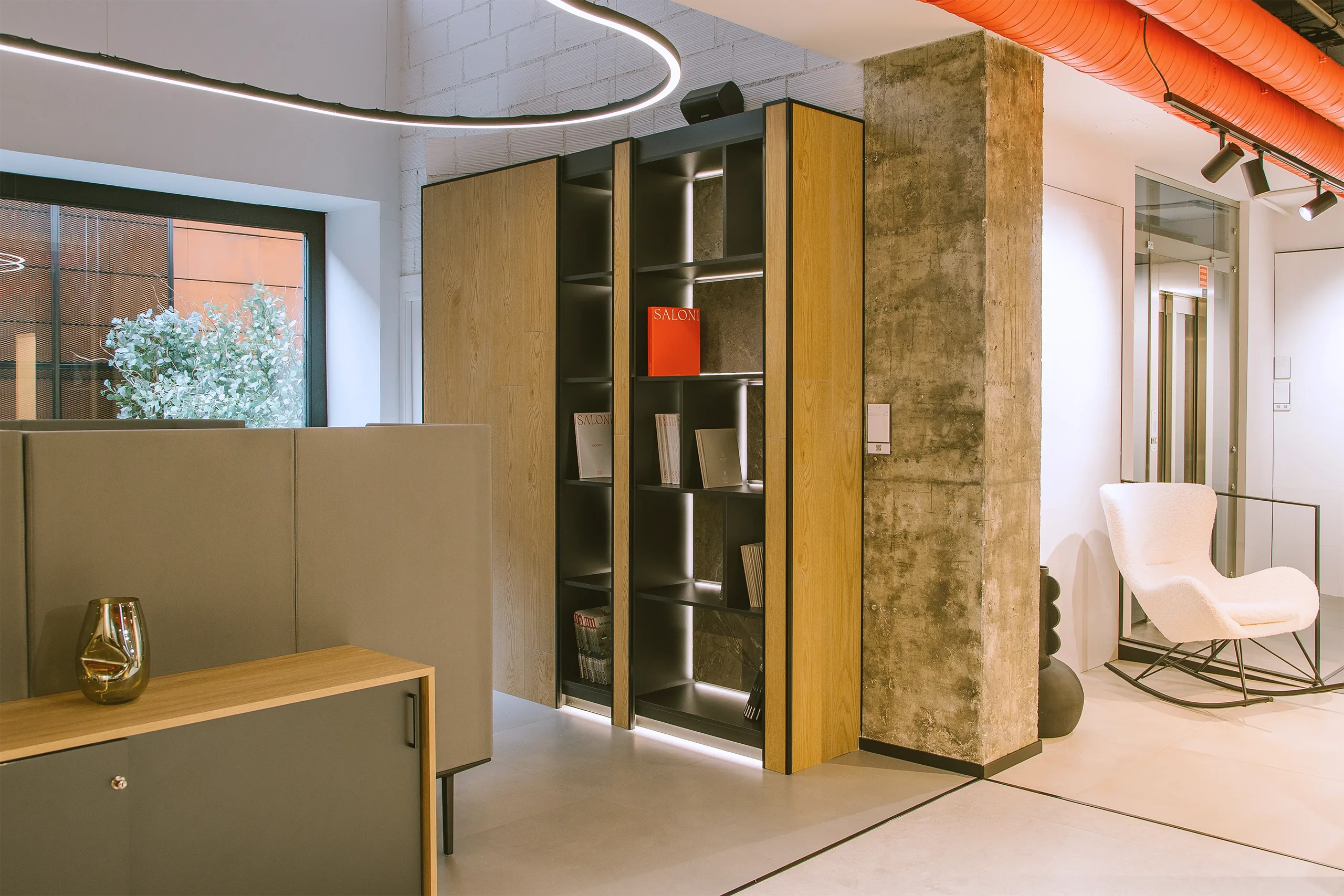 Estantería y mobiliario a medida en showroom SALONI Madrid con catálogos, columna de hormigón visto y butaca de cortesía