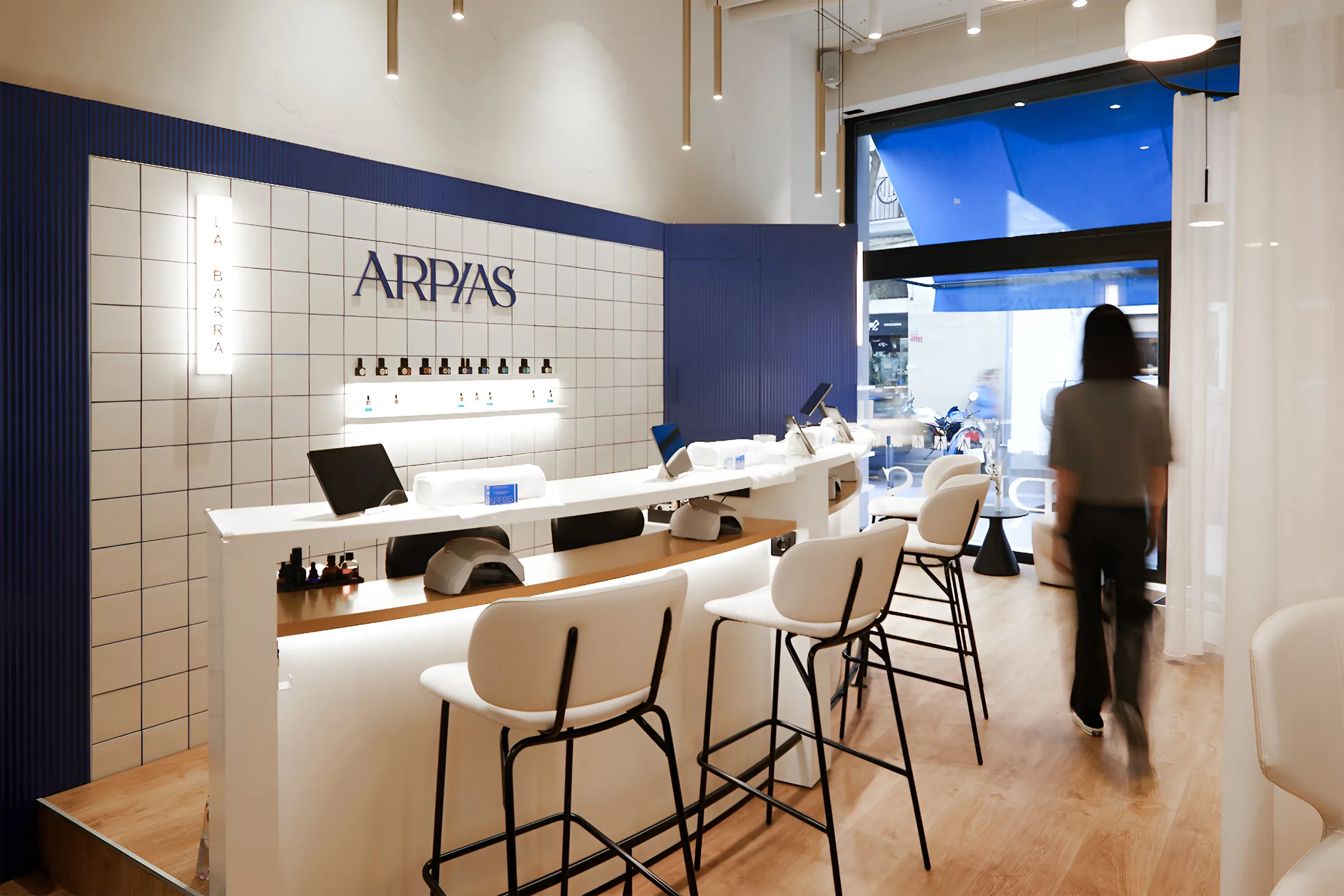 La Barra del salón Arpías en Torrent de l'Olla (Gràcia, Barcelona) con barra curva de manicura, alicatado cerámico blanco con junta azul, paneles acanalados azules y rótulo de marca