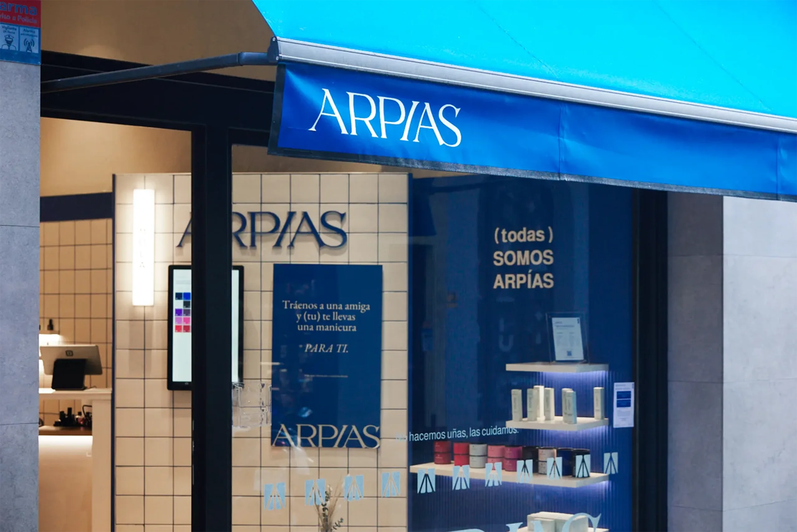Fachada y escaparate de Arpías en Torrent de l'Olla (Gràcia, Barcelona) con alicatado cerámico blanco, rótulo azul, vinilo "(todas) somos Arpías" y producto expuesto, diseñado por huuun