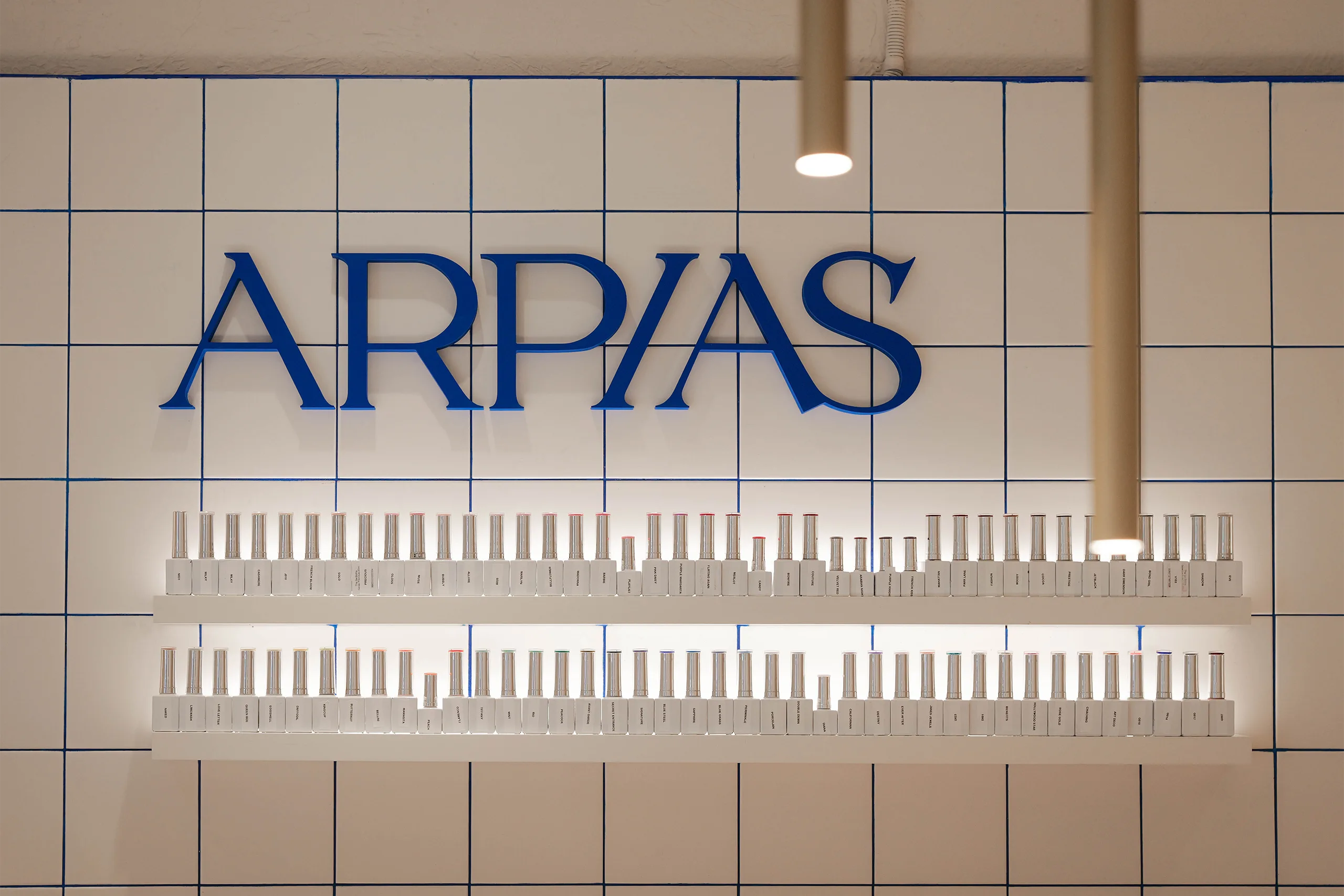 La Barra del salón Arpías en la calle Rubinstein (Putxet, Barcelona) con barra alargada de manicura, taburetes blancos, alicatado cerámico blanco con junta azul y rótulo retroiluminado "LA BARRA"