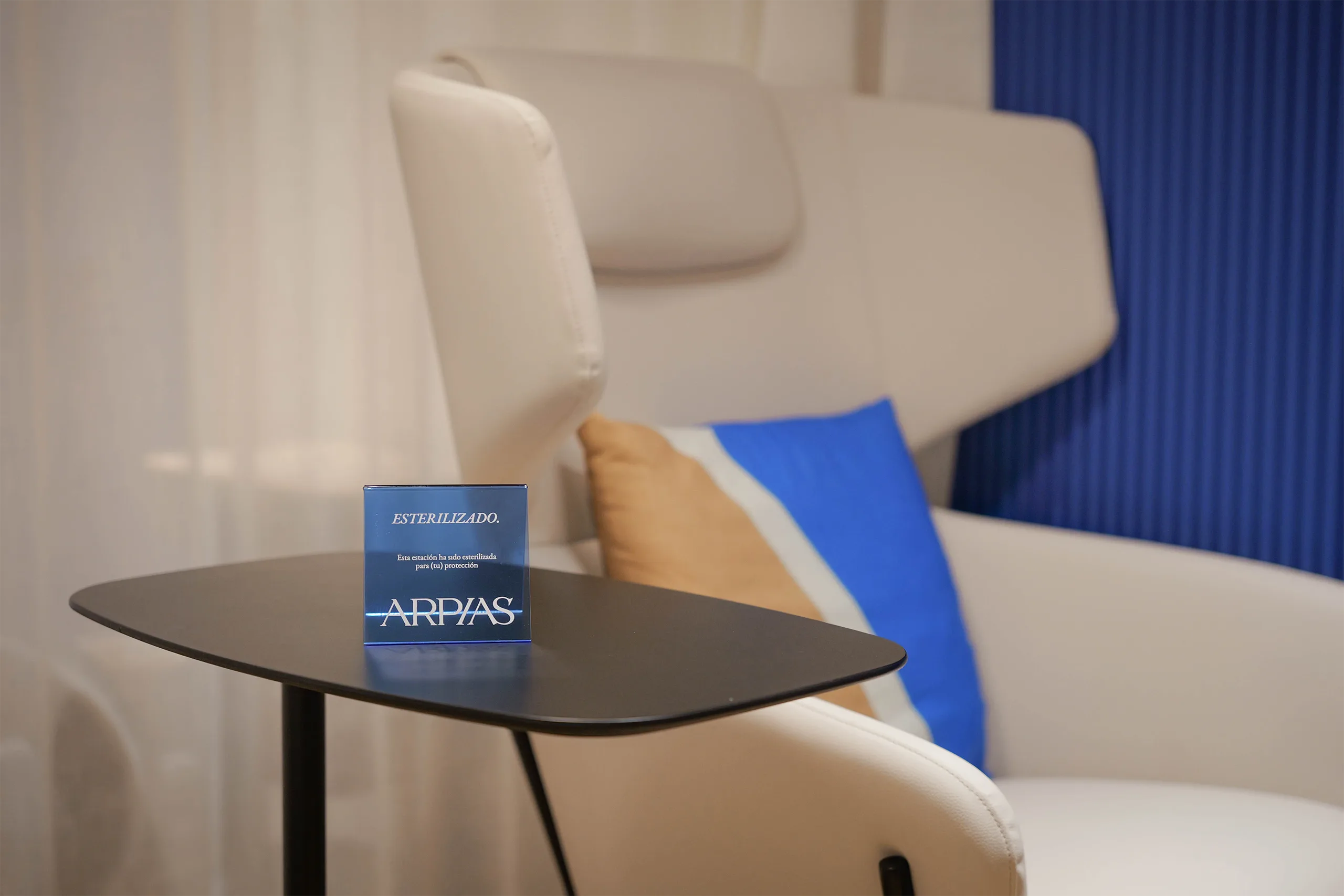 Detalle de mesa auxiliar en La Butaca de Arpías Sant Gervasi (Barcelona) con cartel "Esterilizado", sillón blanco y paneles acanalados azules de fondo