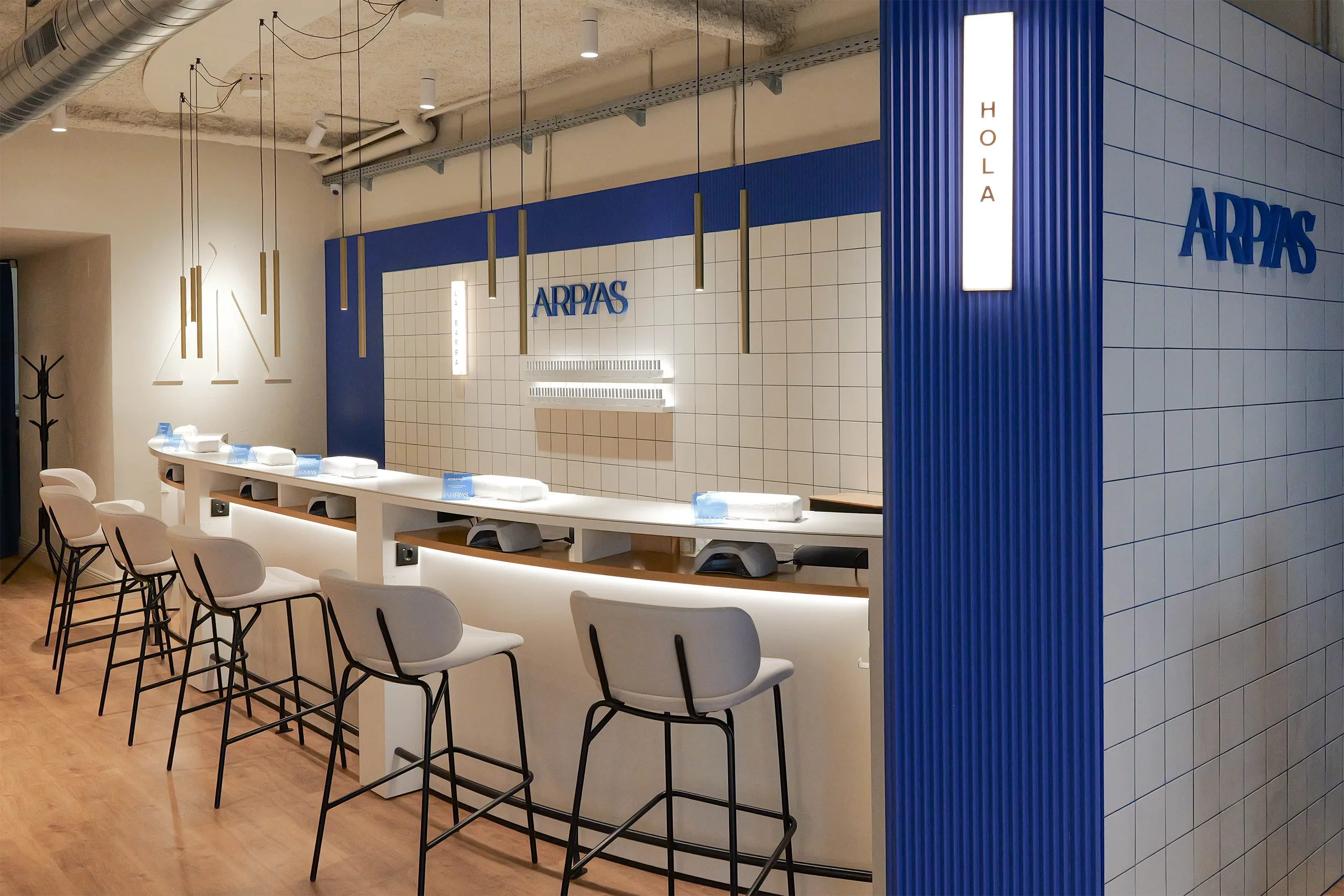 La Barra del salón Arpías en Granada del Penedés (Sant Gervasi, Barcelona) con barra curva de manicura, alicatado cerámico blanco con junta azul, paneles acanalados azules y rótulo de marca