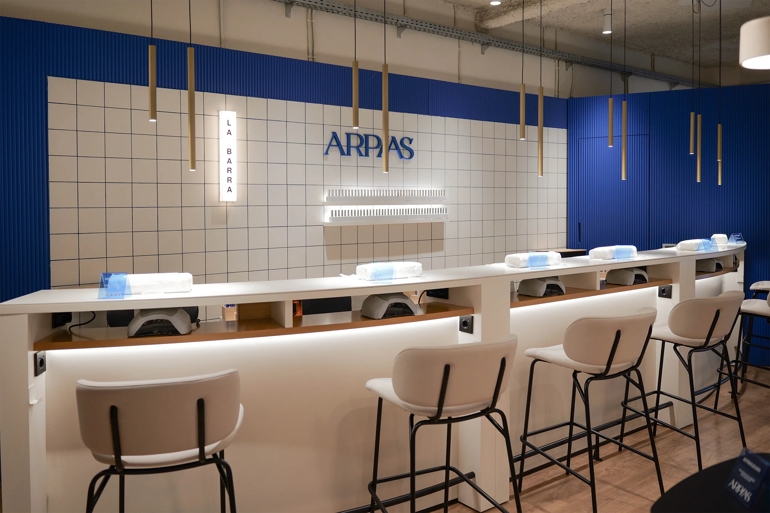 La Barra del salón Arpías en la calle Granada del Penedés (Sant Gervasi, Barcelona) con alicatado cerámico blanco con junta azul, paneles acanalados azules y rótulo "HOLA"