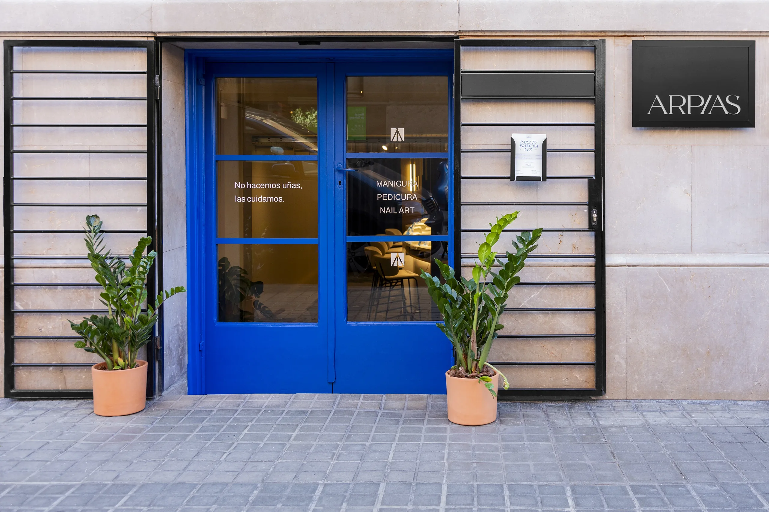 Fachada de Arpías en la calle Madrazo (Sant Gervasi, Barcelona) con puerta de entrada azul intenso, vinilos del salón y vegetación