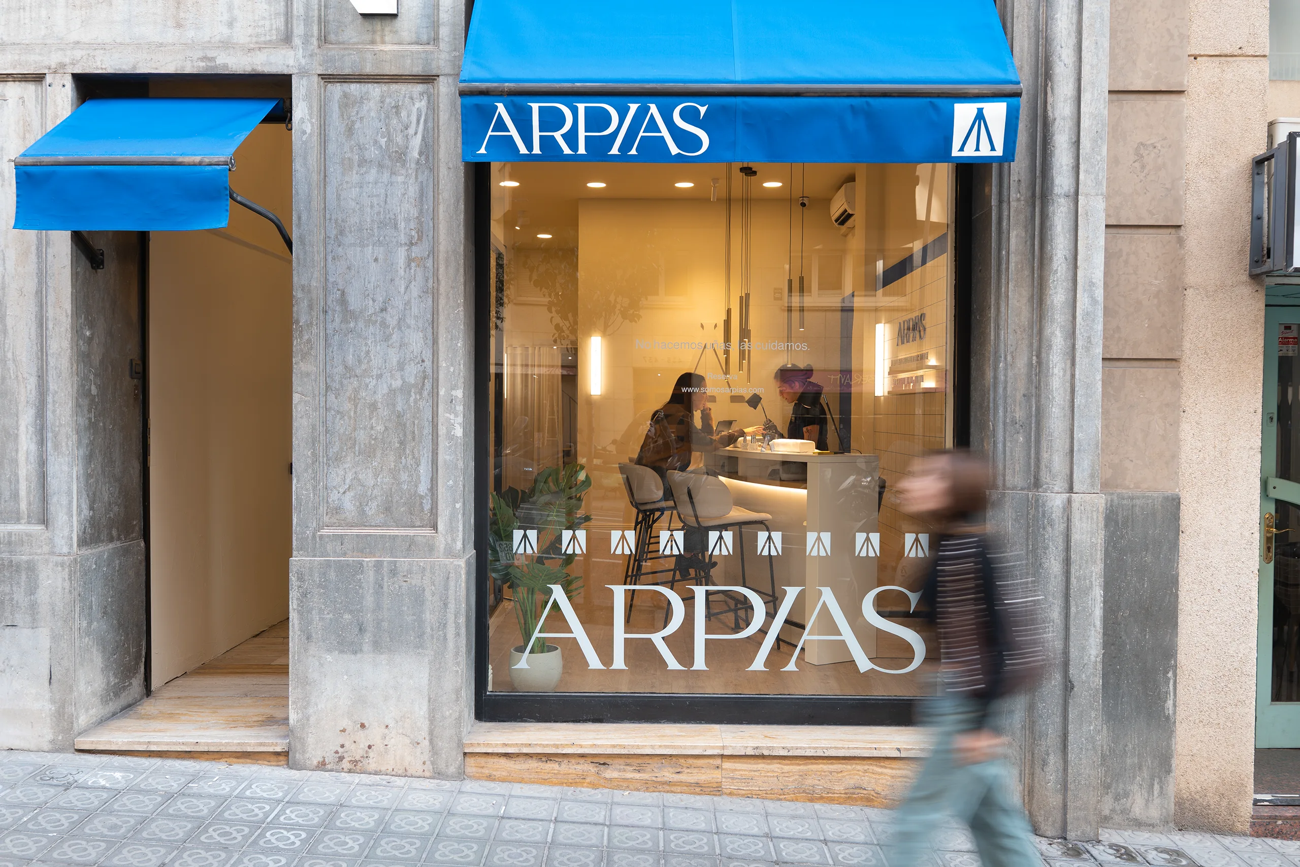 Fachada de Arpías en la calle Muntaner (Sarrià-Sant Gervasi, Barcelona) con toldo azul, vinilo "ARPÍAS" en escaparate, pavimento de panot original y edificio modernista