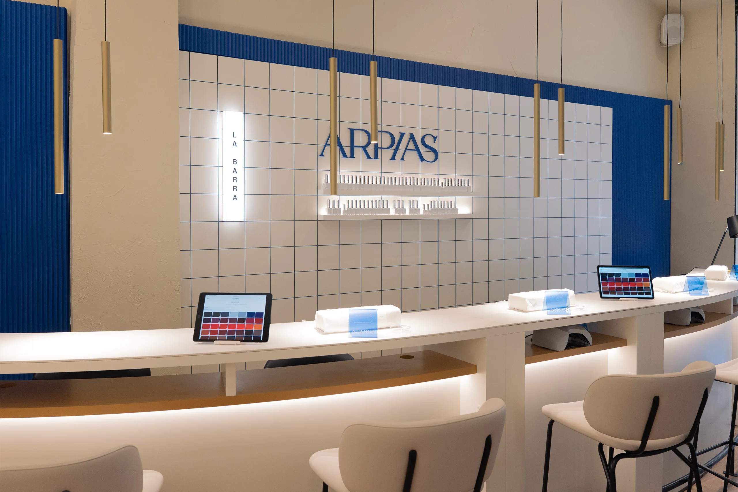 La Barra en Arpías Muntaner (Sarrià-Sant Gervasi, Barcelona) con barra curva de manicura, tablets de selección de color en cada puesto, alicatado cerámico blanco con junta azul y panel acanalado azul lateral
