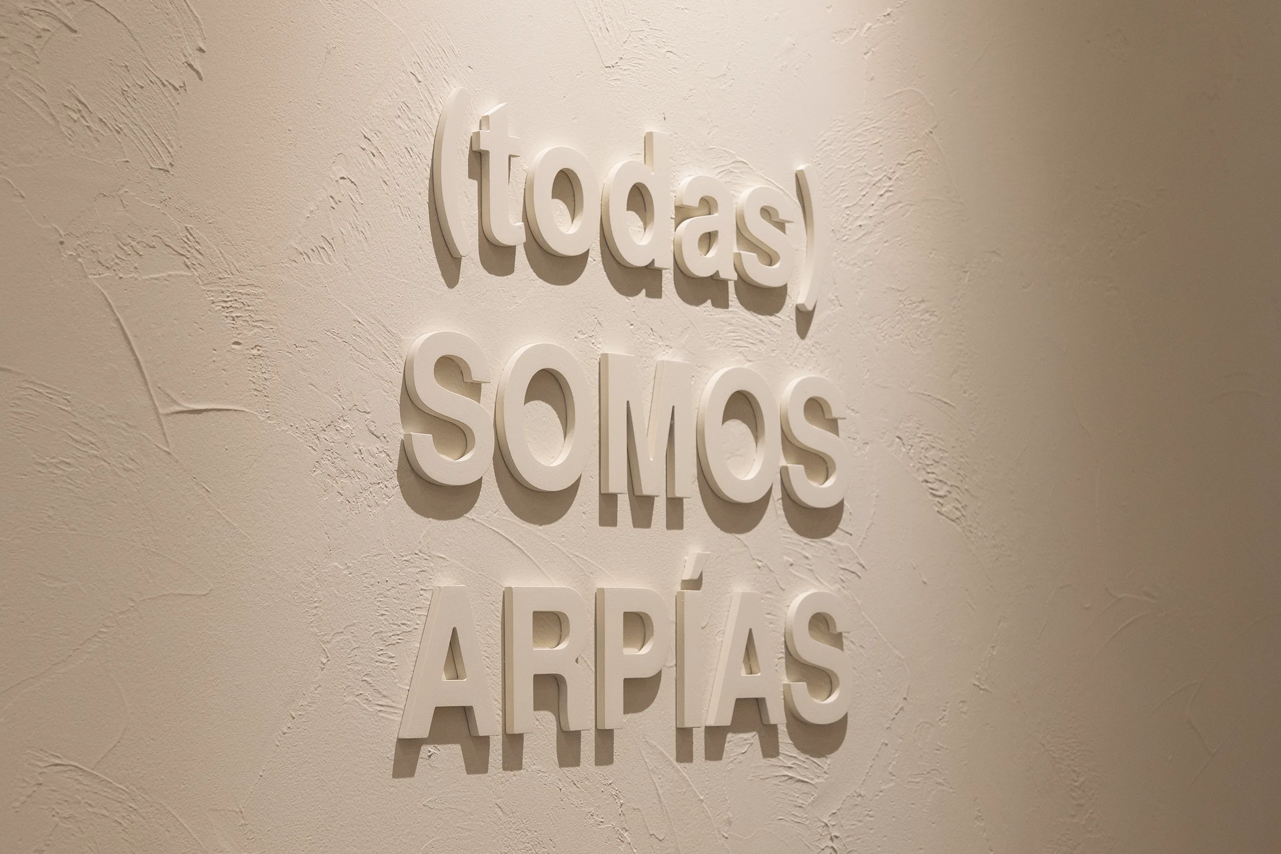 Rótulo "(todas) somos Arpías" en letras corpóreas blancas sobre pared con textura en el salón Arpías de la calle Muntaner (Sarrià-Sant Gervasi, Barcelona)