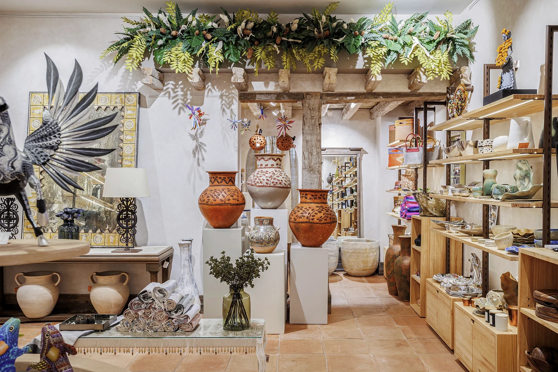 La Galería en Huakal Madrid con vasijas de barro cocido sobre peanas, vigas de madera y instalación vegetal en techo