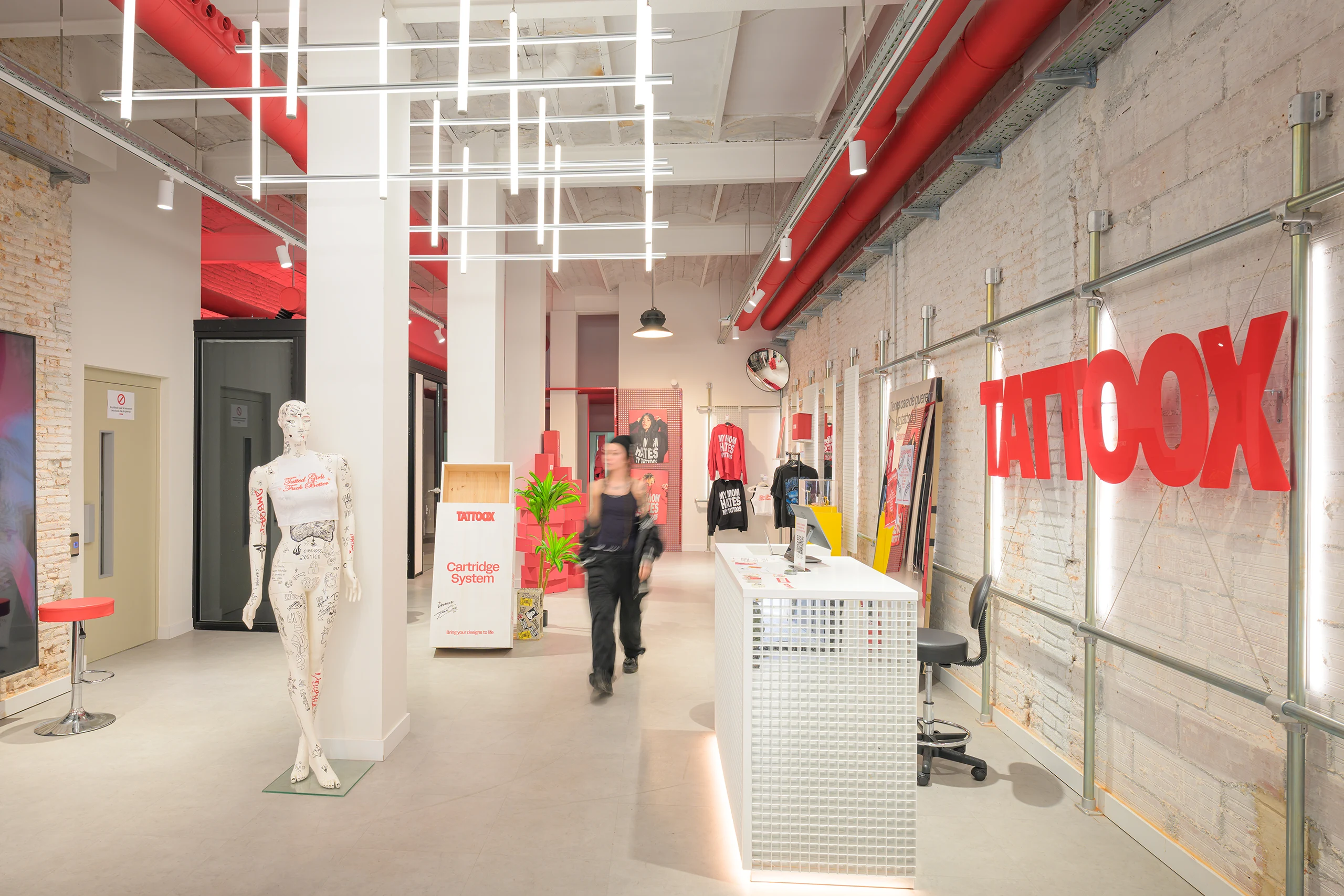 Interior de Tattoox Club Barcelona con muros de ladrillo visto, conductos rojos, iluminación lineal y maniquí tatuado diseñado por huuun