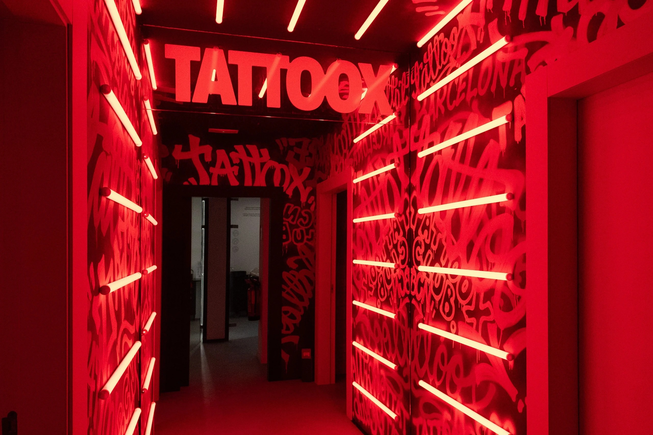 Pasillo inmersivo de Tattoox Club Barcelona con iluminación roja, fluorescentes, gráfica mural tipográfica y rótulo retroiluminado