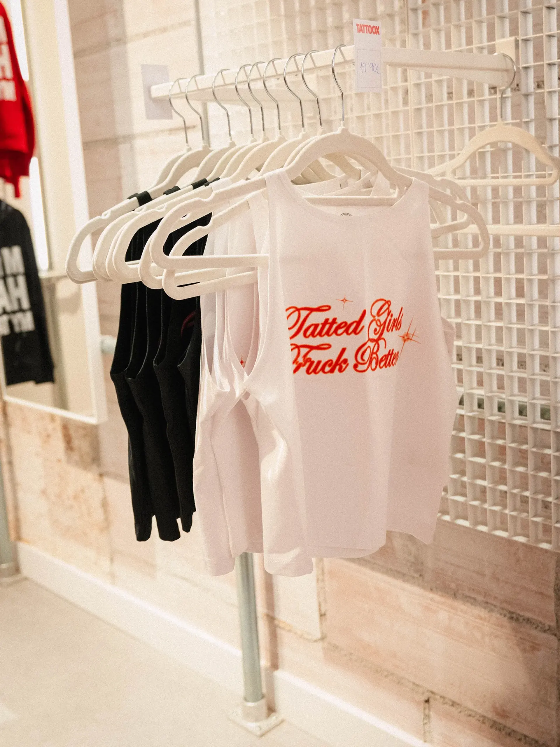Camisetas de la colección de merchandising TattooX colgadas en perchero, con eslogan "Tatted Girls Truck Better" y etiqueta de precio