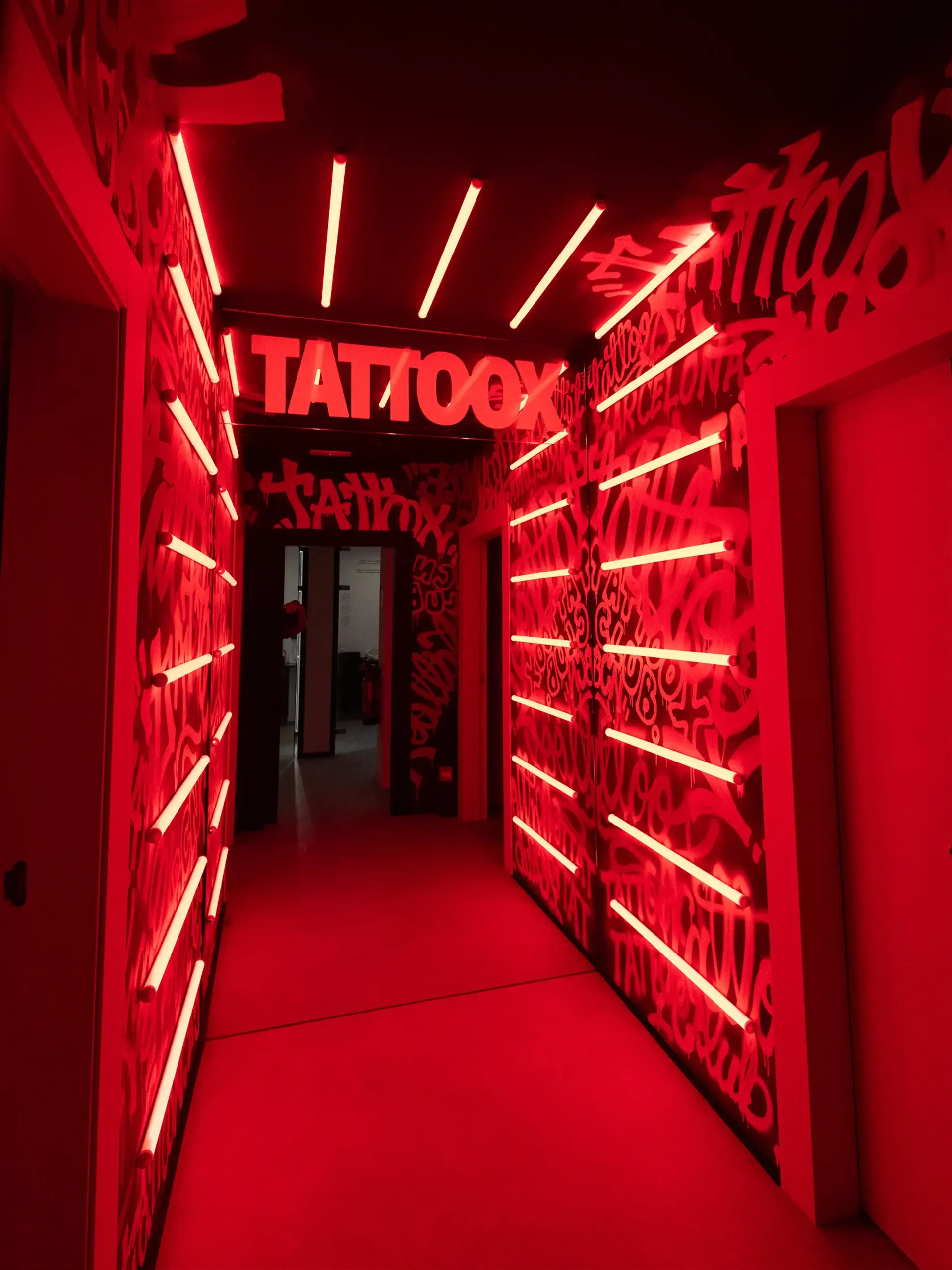 Pasillo de entrada del estudio TattooX con iluminación neón roja y rótulo luminoso "TATTOOX"