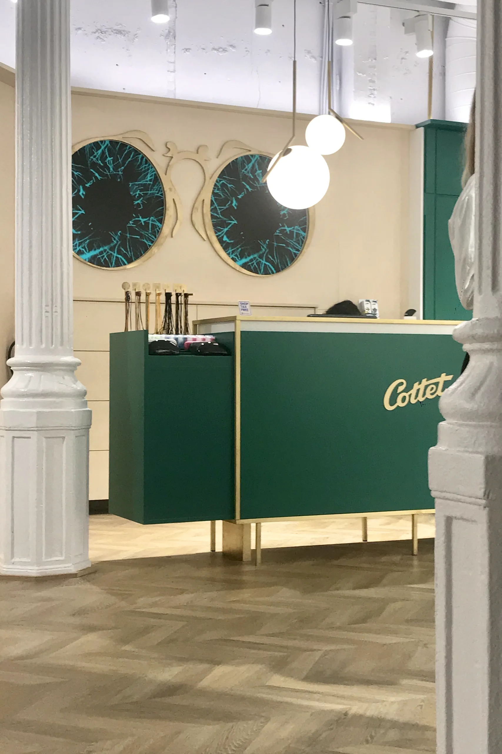 Mostrador de caja Cottet en verde corporativo con logotipo en latón, murales circulares de iris y columnas blancas