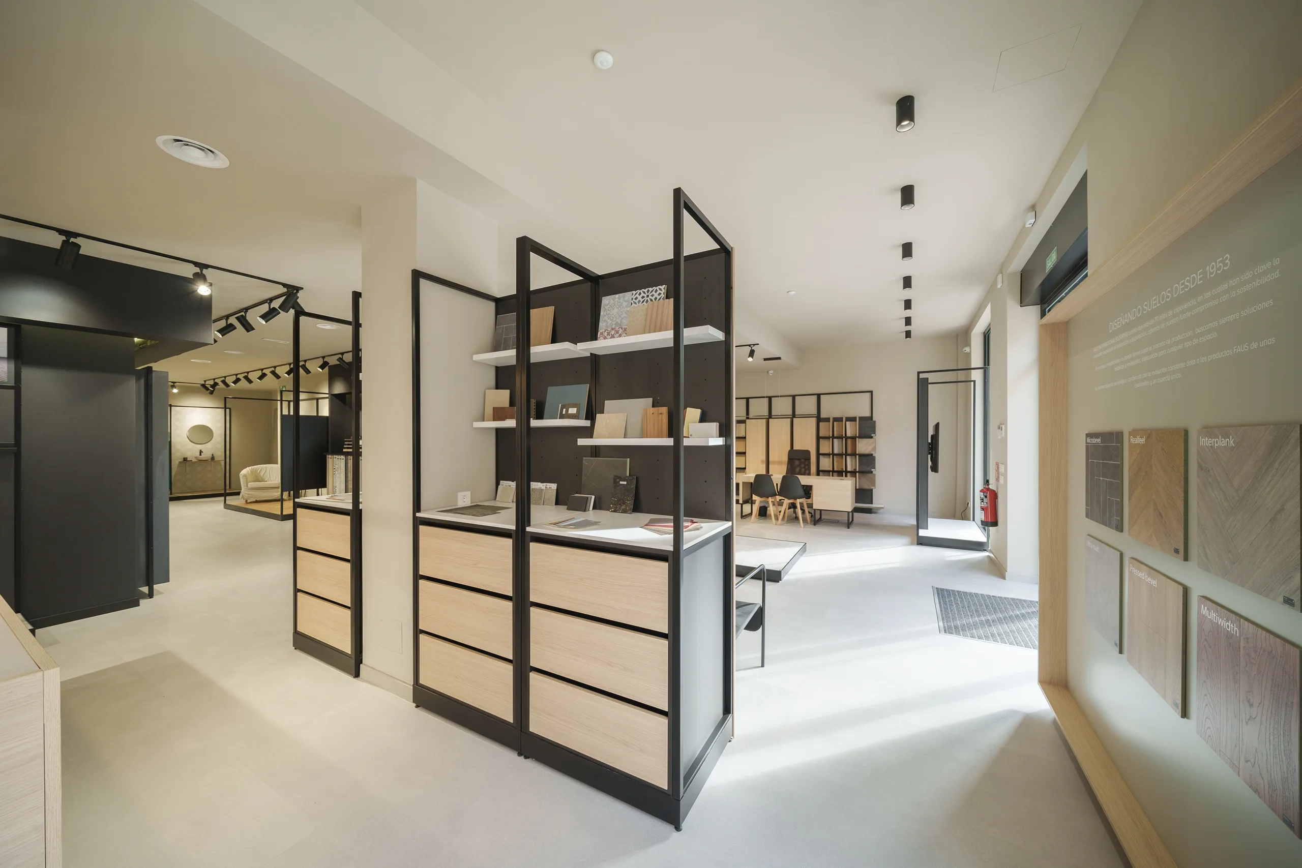 Vista general del showroom FAUS en Madrid con estructura negra continua, módulos expositores de roble y mesa técnica al fondo