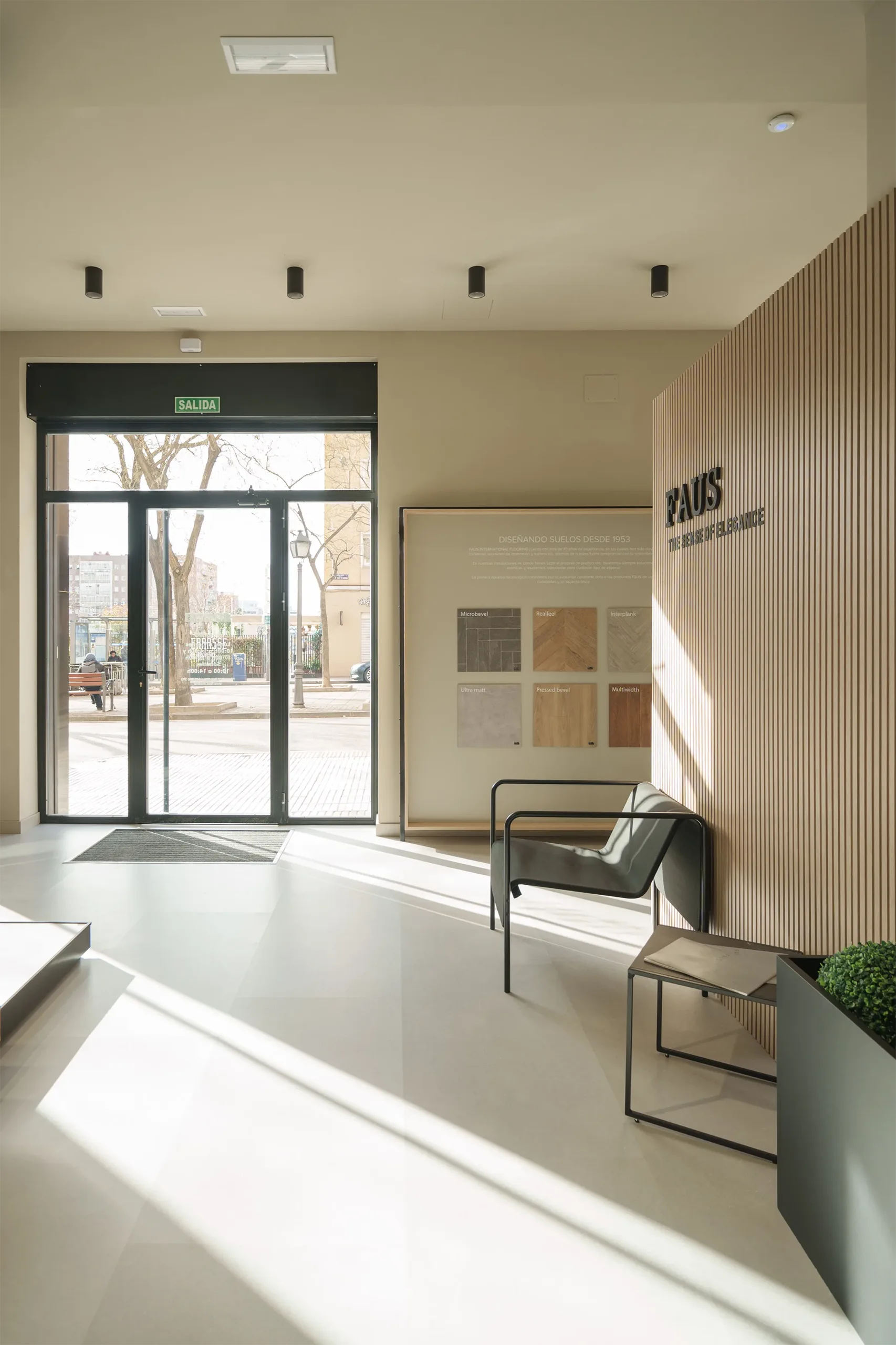 Zona de acceso de la tienda FAUS en Madrid con puerta acristalada, panel corporativo de acabados y muro de lamas