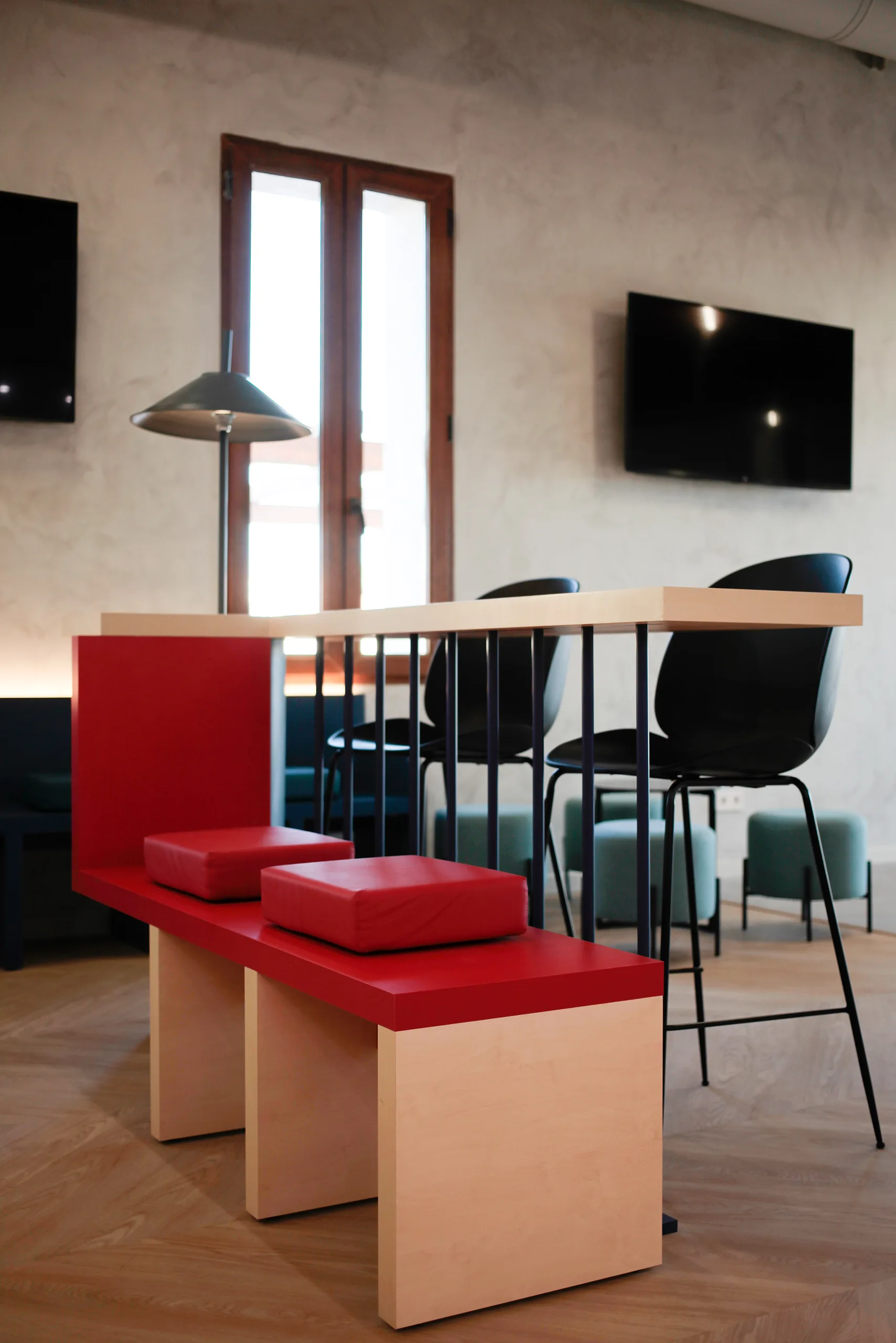 Detalle de banco rojo con cojines y mesa alta con taburetes negros en Key Go Rent! Alicante, junto a ventana de carpintería de madera