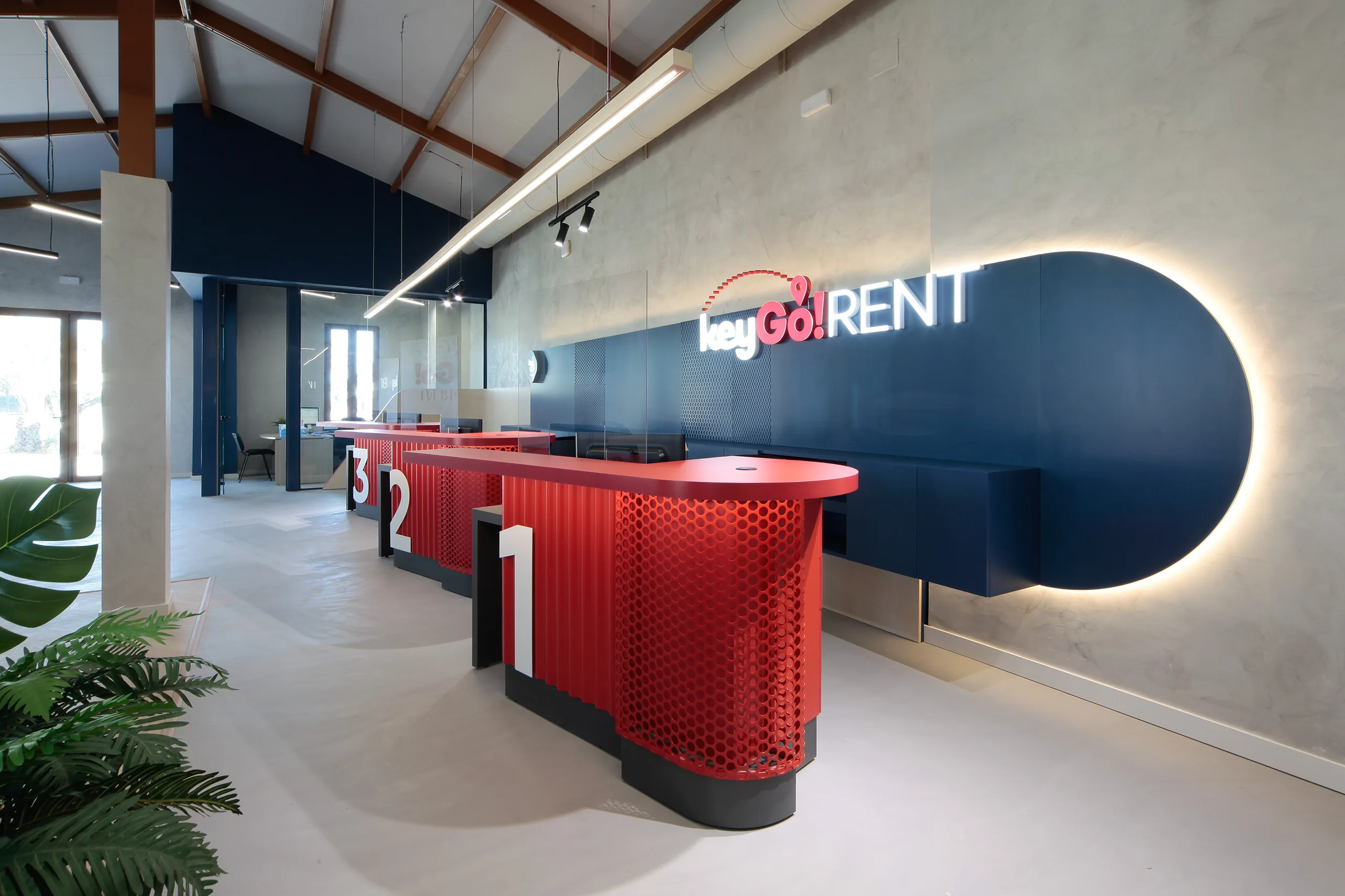 Rincón de espera de Key Go Rent! Alicante con arco luminoso rojo, banco curvo y cerramiento de chapa azul petróleo