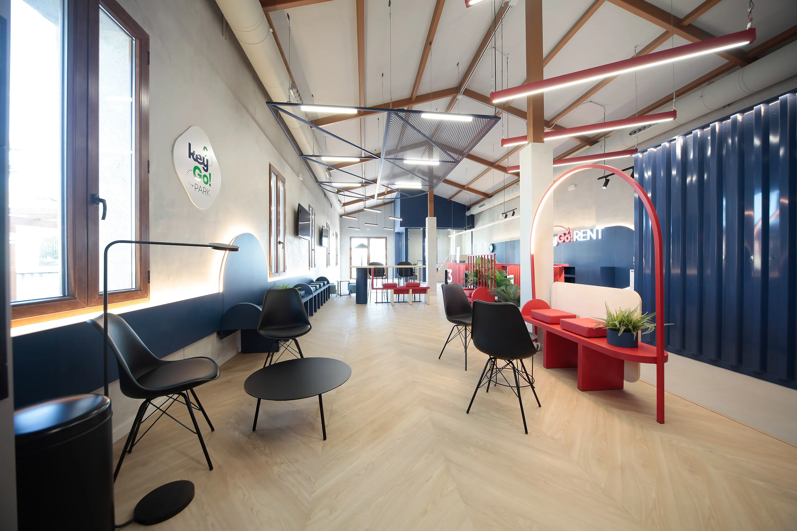 Zona de espera de Key Go Rent! en Alicante con banco rojo, arco luminoso, chapa azul petróleo y suelo en espiga
