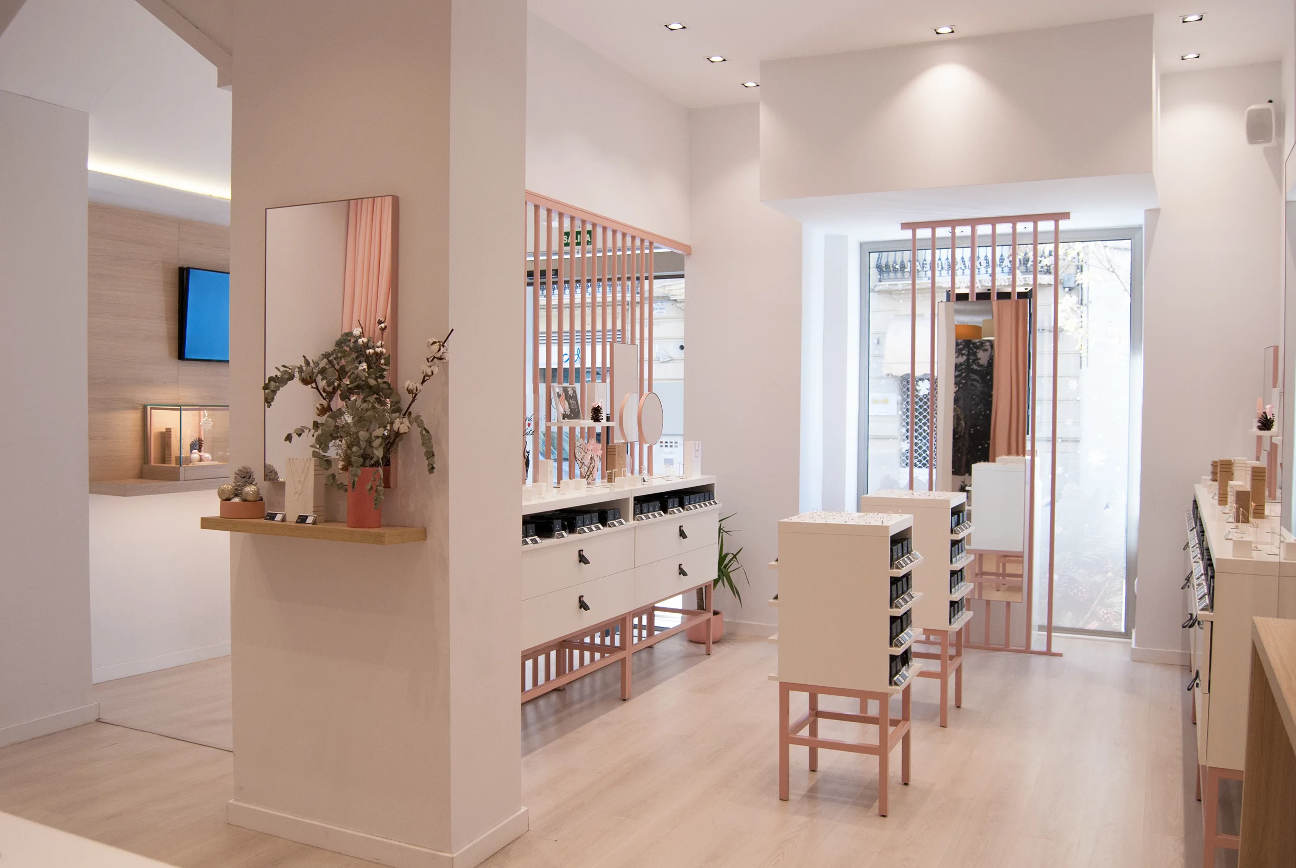 Vista general de tienda Singularu con columna blanca, celosías rosas, expositores blancos de patas rosas y escaparate con luz natural